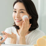 40代女性が泡で洗顔し、潤った肌を確認する様子。背景に#肌をメイクする石鹸と保湿成分のボトルが映る。