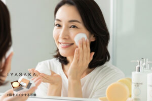 40代女性が泡で洗顔し、潤った肌を確認する様子。背景に#肌をメイクする石鹸と保湿成分のボトルが映る。