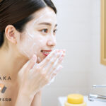 泡で洗顔する女性。背景に#肌をメイクする石鹸が置かれたバスルーム