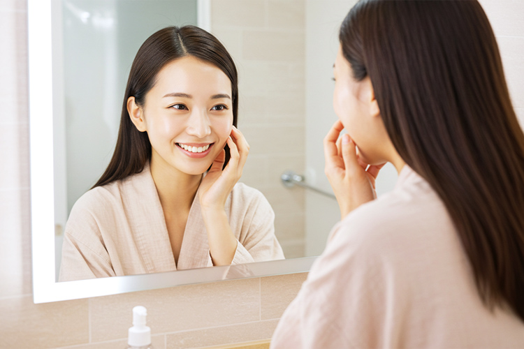 鏡の前で笑顔で肌を確認する日本人女性。肌がつやつやで健康的。