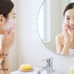 笑顔の女性が泡で洗顔するシーン。背景に#肌をメイクする石鹸が置かれたバスルーム