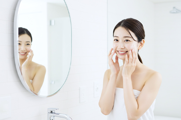洗顔後のツヤツヤの肌を触りながら笑顔で立っている女性