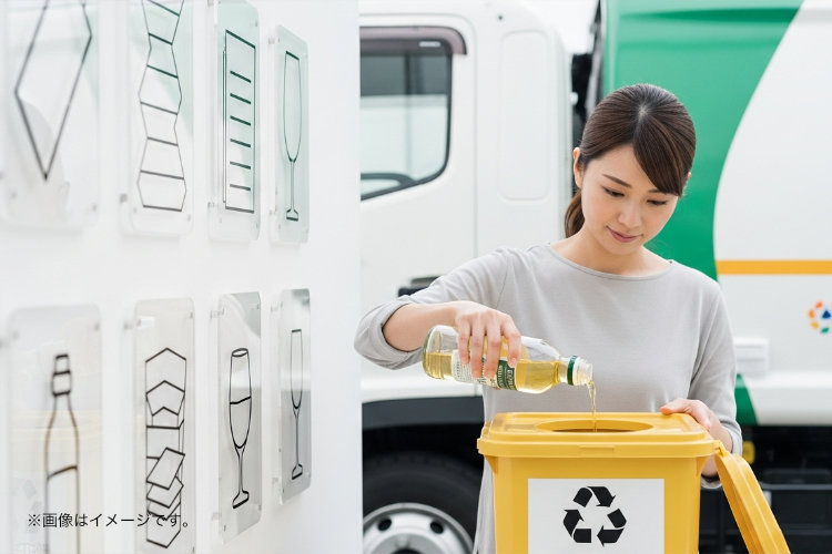 日本人女性が廃油を専用の容器に入れている。背景にリサイクルマークとゴミ収集車。